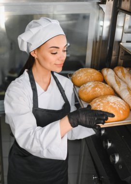 Siyah eldiven giyen profesyonel fırıncı ticari bir fırından bir tepsi taze ekmek alıyor.