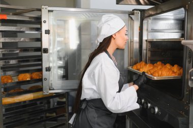 Profesyonel fırıncı üniformalı, ticari bir fırında büyük bir fırından yeni pişmiş kruvasan alıyor.