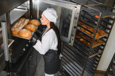 Profesyonel fırıncı bir fırında, bir tepsi taze pişmiş ekmeği ticari bir fırından çıkarıyor.