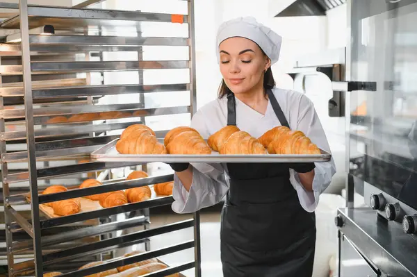 Profesyonel fırıncı gururla sunar bir tepsi altın kahverengi kruvasan, bir fırın ortamındaki uzmanlığının sonucunu sergiliyor