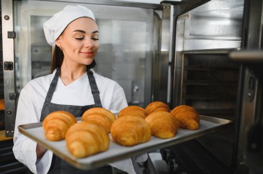 Profesyonel bir fırıncı taze pişmiş altın kruvasan kokusu alıyor. Elinde ticari bir mutfakta tepsi tutuyor.