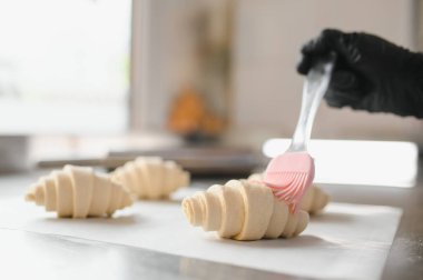 Baker, profesyonel mutfakta pişirmeden önce taze kruvasanlara yumurta banyosu yapan silikon fırça kullanıyor.