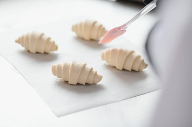 Pasta şefi spatula kullanarak taze pişmiş kruvasanları canlı pembe kremayla parlatıyor, fırında hünerlerini ve yaratıcılıklarını sergiliyor.