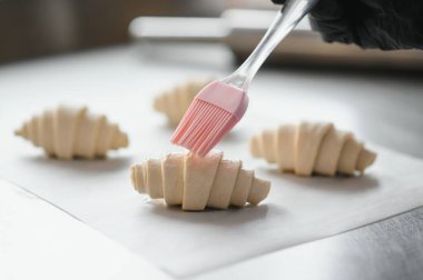 Silikon hamur fırçası kullanarak kruvasanları yumurta yıkama ile kaplamak, hamur işlerini pişirmek için hazırlamak.