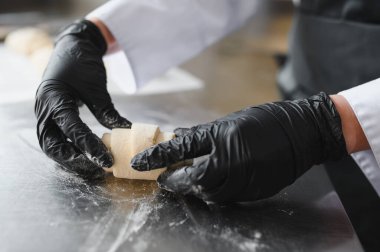 Fırıncı, siyah eldivenleri ustalıkla giyip fırın mutfağında altın rengi kahverengi bir kruvasan hazırlıyor ve şekillendiriyor.