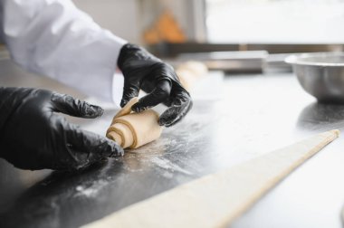 Siyah eldivenler giyen fırıncı profesyonel mutfakta paslanmaz çelik masada kruvasan hamuru hazırlıyor.