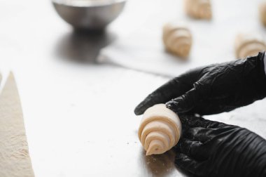 Fırıncı eldiveni giyip kruvasanları fırının mutfağında paslanmaz çelik bir masada hazırlıyor.