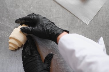 Siyah eldiven giyen fırıncı profesyonel mutfakta lezzetli kruvasanlar hazırlıyor. Hamur işlerinde ustalık ve uzmanlık gösteriyor.