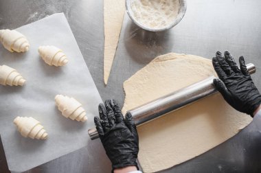 Hamuru düzleştirmek için merdaneyi ustaca kullanmak, lezzetli aromalarla dolu fırın mutfağında taze kruvasan pişirmek.