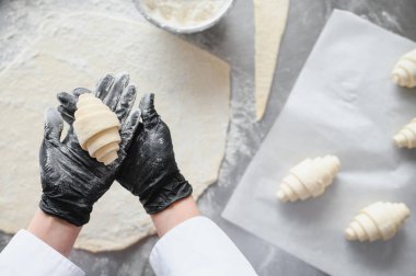 Siyah eldiven giyen fırıncı fırında yeni yapılmış bir kruvasanı gururla sunar. Hamur işi yaratma sanatını ön plana çıkarır.