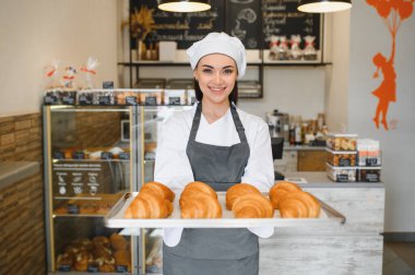 Gülümseyen fırıncı fırınında bir tepsi altın rengi kruvasan sunuyor, lezzetli hamur işlerini gösteriyor.