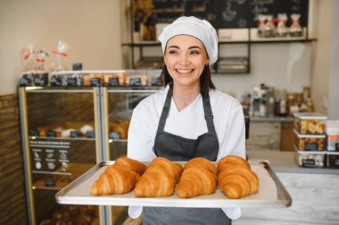 Gülümseyen fırıncı bir tepsi altın kruvasan sunarak fırınının ürünlerinin kalitesini ve tazeliğini gözler önüne seriyor.