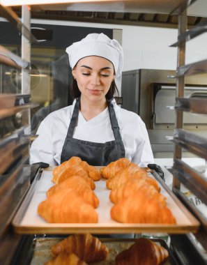 Profesyonel fırıncı dikkatli bir şekilde altın kahverengi kruvasan tepsisini endüstriyel fırına yerleştiriyor ve modern fırında mükemmel pişirme sağlıyor.