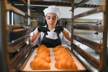 Profesyonel fırıncı soğutma rafında bir tepsi altın-kahverengi kruvasan hazırlıyor, hava akımını ve mükemmel dokuyu sağlama alıyor.