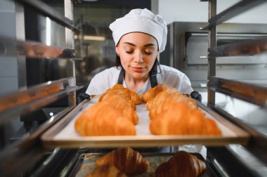 Profesyonel fırıncı taze kruvasan kokusu alıyor, fırındaki tepsiyi çıkarıyor.