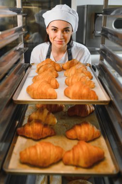 Profesyonel fırıncı, mükemmel altın rengi kruvasanlardan oluşan tepsileri sunar. Bir fırında pişirme uzmanlığının sonucunu gözler önüne serer.