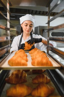 Profesyonel bir fırıncı, ticari bir mutfakta yemek tepsileri üzerine altın sarısı kruvasanlar yerleştiriyor. Kaliteyi ve sunumu garantiliyor.