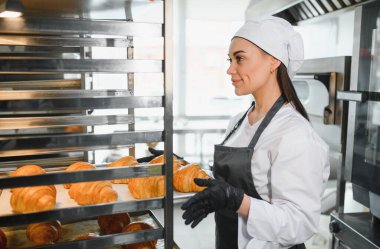 Profesyonel fırıncı, ticari mutfağın soğutma rafına altın rengi kruvasan koyuyor.