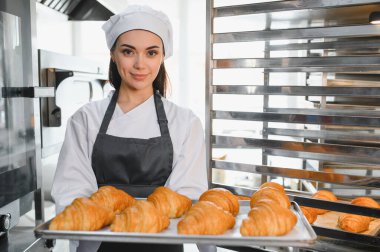 Profesyonel fırıncı bir tepsi altın kruvasan sunuyor. Fırınının kalitesini ve uzmanlığını gösteriyor.