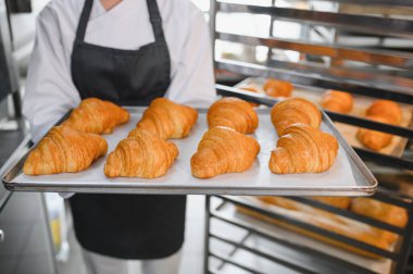 Fırıncı tepsisi altın sarısı kruvasan sunuyor, profesyonel mutfakta pişirmenin sonucunu gösteriyor.