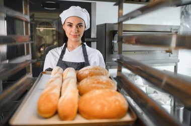 Profesyonel fırıncı bir tepsi baget ve yuvarlak somun sunar, bir fırında yaptığı çalışmaların sonucunu sergiler.