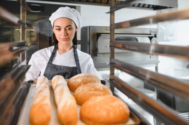 Kadın fırıncı fırın mutfağındaki metal soğutma rafında ekmek ve baget düzenliyor.