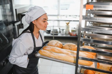 Profesyonel bir fırıncı, ticari bir fırının rafına taze ekmek tepsisi koyar, aromasını ve sanatsal ekmeğin kalitesini gösterir.