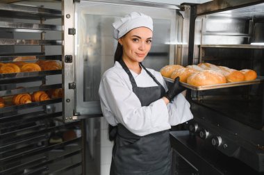 Profesyonel fırıncı bir fırında, bir tepsi taze pişmiş ekmeği ticari bir fırından çıkarıyor.