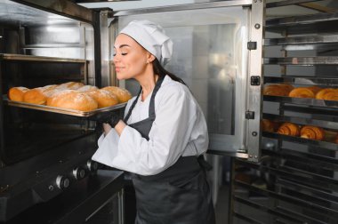 Fırıncı fırında çalışan fırından altın bir somun çıkarırken taze ekmek aromasının tadını çıkarıyor.