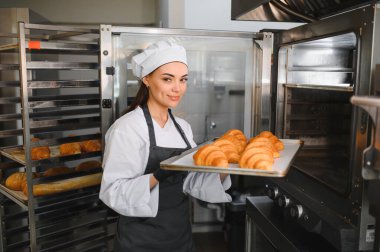 Profesyonel fırıncı ticari fırındaki büyük sanayi fırınına altın rengi kruvasan tepsisi koyar.