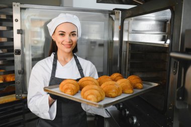 Profesyonel fırıncı gülümsüyor ve fırında pişmiş altın kruvasan tepsisini fırının önünde tutuyor.