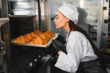 Mutluluktan kokan profesyonel fırıncı kadın fırından yeni çıkarılmış bir tepsi altın kruvasan.