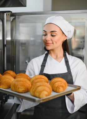 Profesyonel fırıncı gururla sunar bir tepsi altın kahverengi kruvasan, onun fırınlanmış ürünlerinin kalitesini ve lezzetini sergiliyor