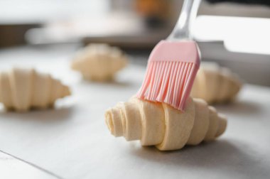 Fırıncı çiğ kruvasanlara yumurta yıkama, altın rengini arttırma ve onları fırına hazırlama, lezzetli bir kahvaltı hazırlama