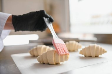 Fırıncı yeni pişmiş kruvasanlara silikon fırçayla jöle sürüyor, profesyonel mutfakta lezzetli hamur işleri hazırlıyor.