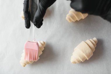 Silikon hamur fırçası kullanarak kruvasanları yumurta yıkama ile kaplamak, hamur işlerini pişirmek için hazırlamak.