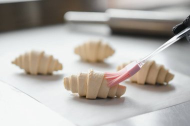 Fırıncı kruvasanları pişirmeden önce yumurta yıkama ile kaplıyor, lezzetli kahverengi hamur işleri yaratıyor.