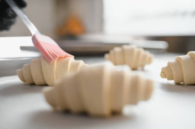 Fırıncı kruvasanları yumurta banyosuyla kaplıyor. Güzel bir altın kabuk oluşturuyor. Mutfakta lezzetli bir fırına hazırlanıyor.