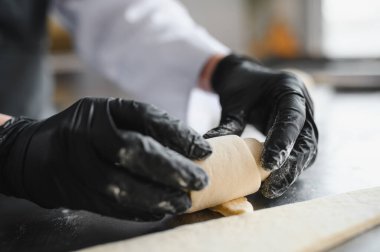 Siyah eldiven giyen fırıncı hamuru mükemmel bir silindirde yuvarlıyor ve lezzetli kruvasanlar yapmaya hazırlanıyor.