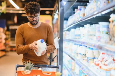 Bir süpermarkette mandıra reyonunda alışveriş yaparken süt şişesi etiketini inceleyen genç adam sağlıklı seçimler yapmaya odaklanmış.