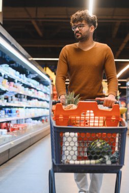 Müşteri market koridorunda yürürken ve ürünleri seçerken alışveriş arabasını itiyor.