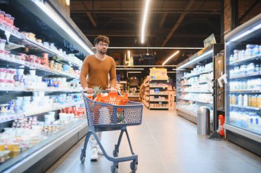 Markette alışveriş arabalarını iten genç bir Arap adam market alışverişi yaparken, dondurucu koridorlarda yürürken