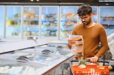Müşteri önceden paketlenmiş donmuş balığı süpermarket buzdolabı koridorunda seçiyor, alışveriş arabasını itiyor.