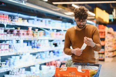 Genç adam süpermarkette alışveriş yaparken market fişini kontrol ediyor. Bütçeyi aşmadığından emin oluyor.