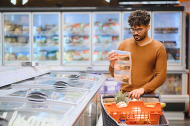 Müşteri dondurulmuş balığı süpermarketin buzdolabı bölümünden seçiyor, alışveriş arabasını market alışverişiyle dolduruyor.