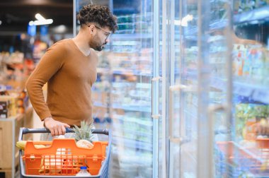 Müşteri dondurulmuş gıdayı süpermarkette dondurulmuş bir reyondan seçiyor, taze ürünlerle dolu bir alışveriş arabasını itiyor.