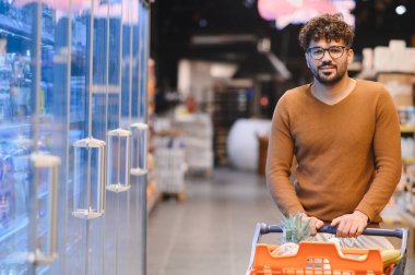 Müşteri alışveriş arabasını iterken markette taze yiyecekler seçiyor, hareketli bir alışveriş deneyiminin tadını çıkarıyor.