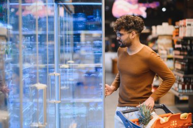 Genç bir adam markette dondurulmuş bir koridordan alışveriş arabasıyla alışveriş yapıyor.