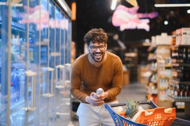 Mutluluktan kahkahalar atan bir müşteri marketin buzdolabı bölümünde alışveriş arabasını iterken.