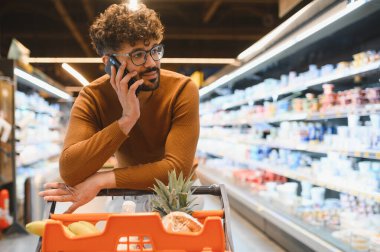 Müşteri marketten alışveriş yaparken telefon ediyor, taze ve sağlıklı ürünler seçiyor.